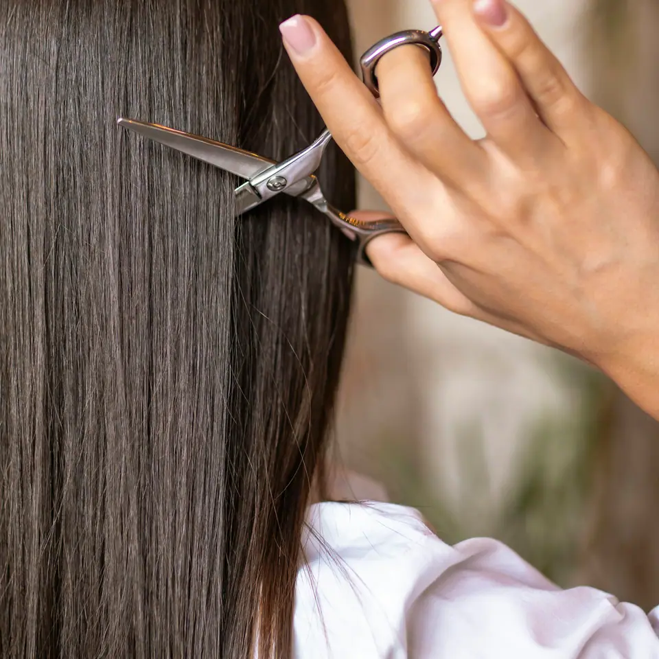 Une coiffeuse coupe une longue chevelure brune aux ciseaux.