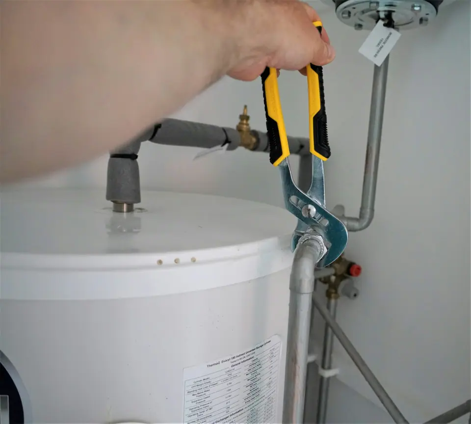 Une main serre le raccord d’un chauffe-eau avec une pince.